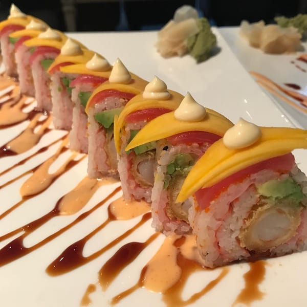 A row of Bonsai Thai & Sushi rolls with mango, tuna, avocado, and shrimp tempura, drizzled with sauces.