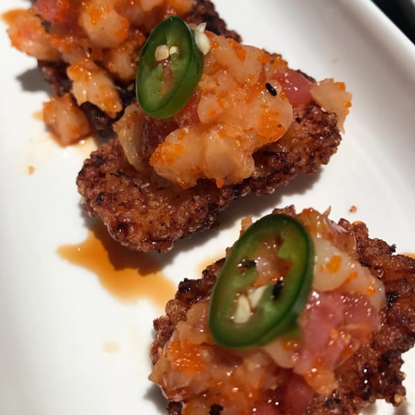 Three crispy rice sushi appetizers topped with spicy tuna, orange roe, and a green jalapeño slice.